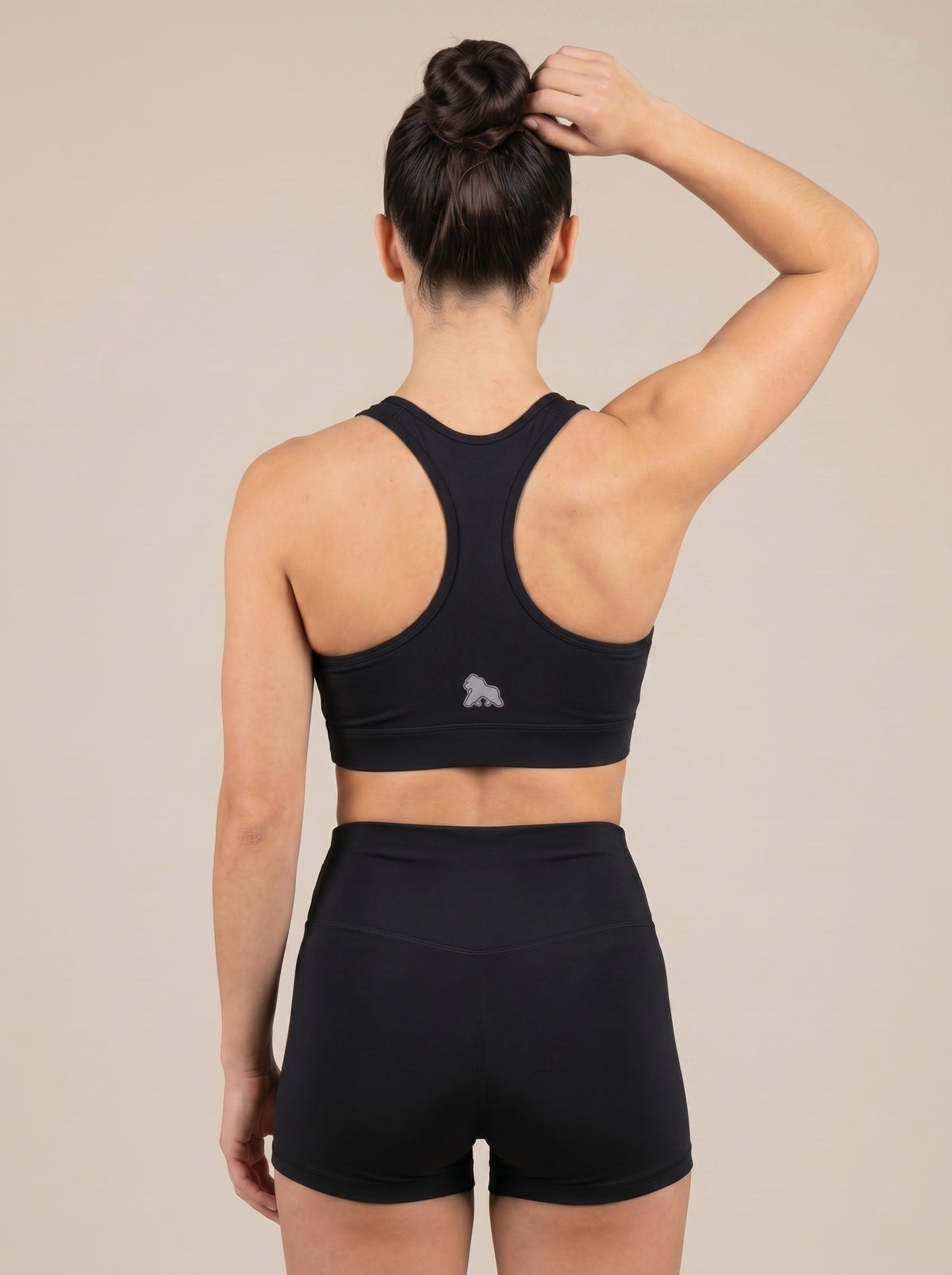 Model wearing a black FIT APE sports bra with one arm raised, back view