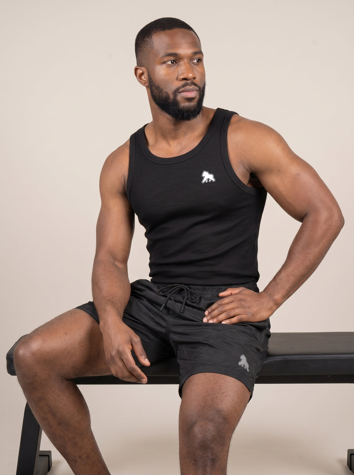 Seated model wearing a black FIT APE men's tank top with white chest gorilla
