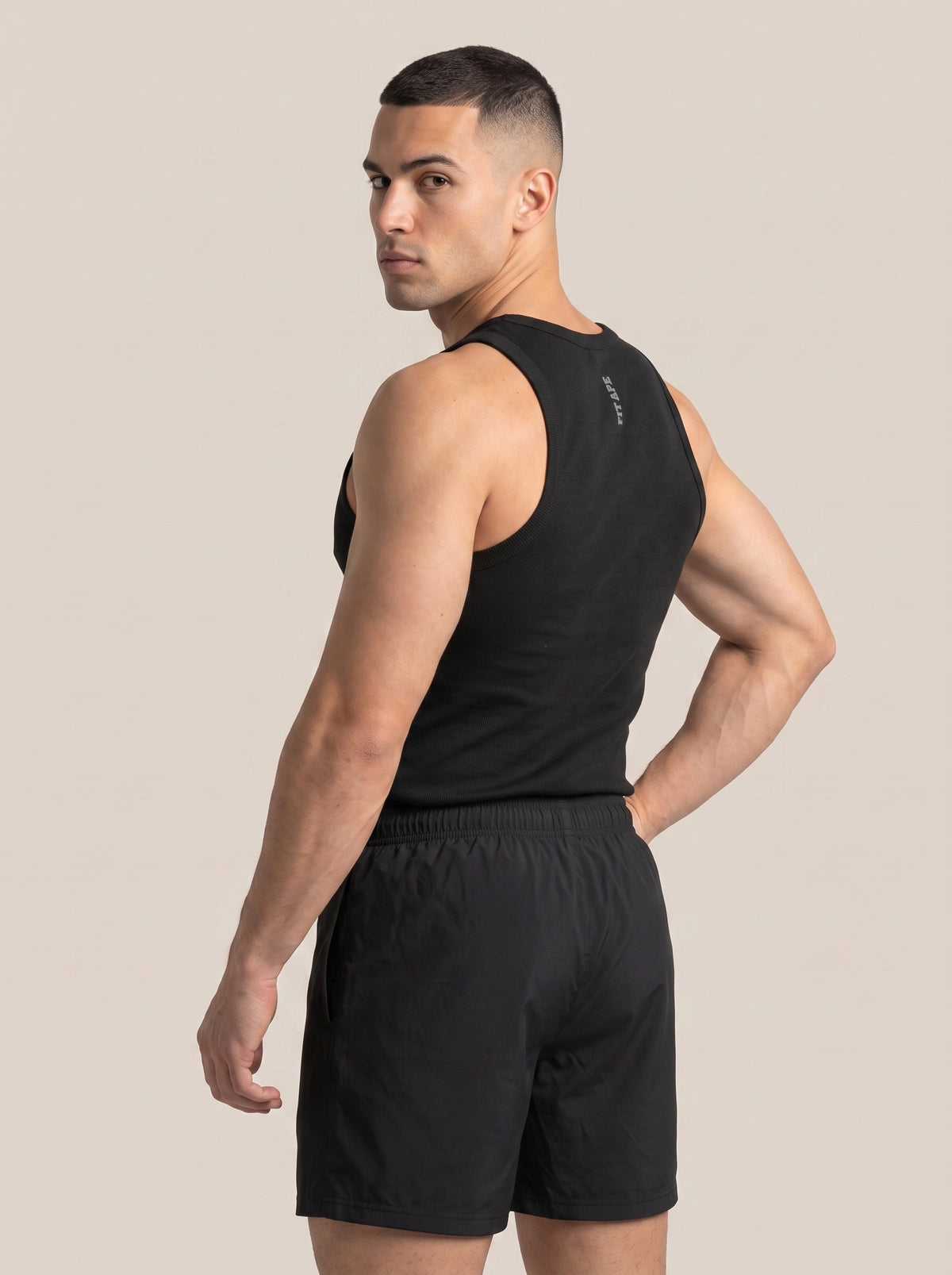 Model wearing a black FIT APE men's tank top, rear three-quarter view