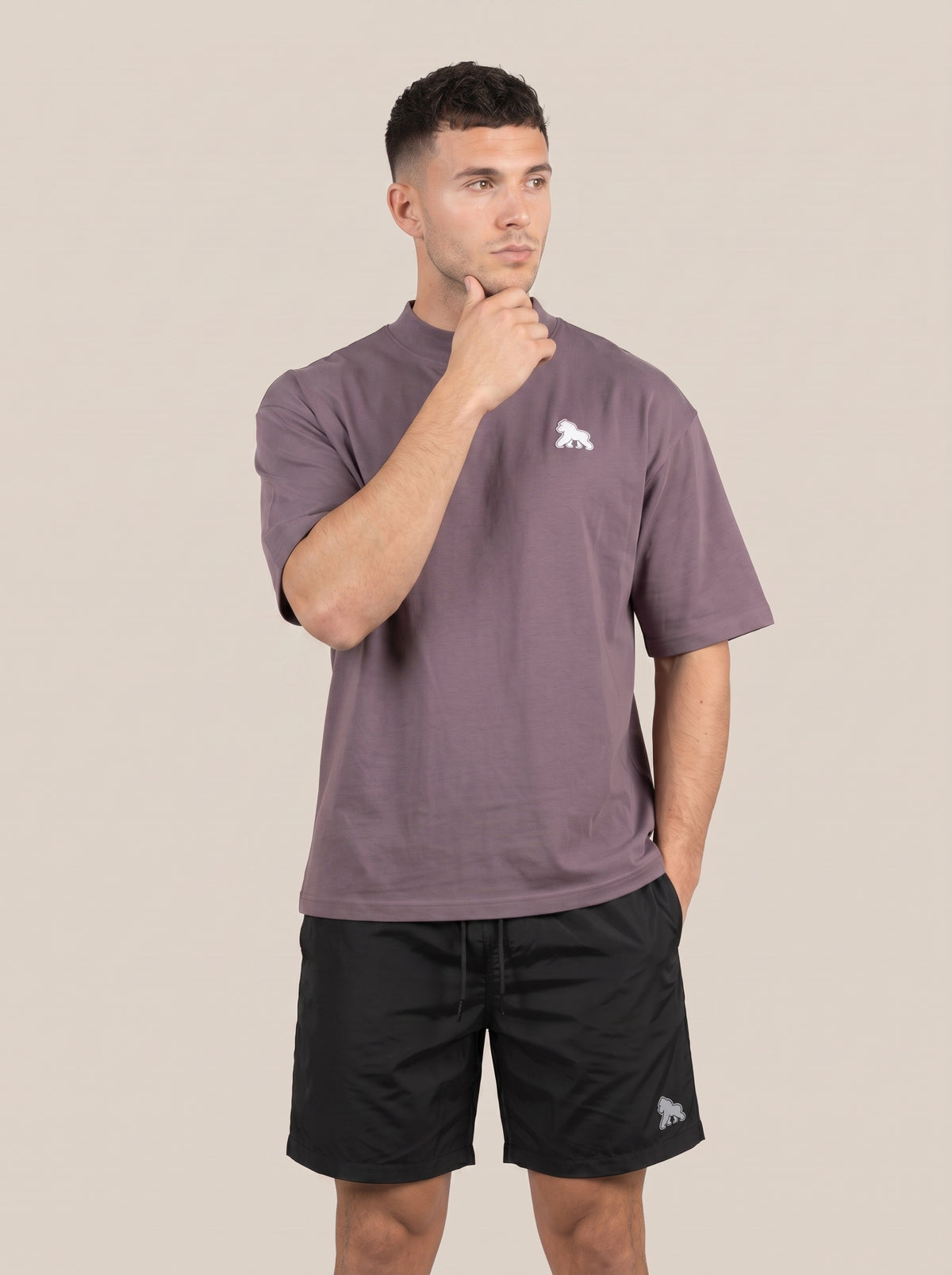 Muted purple FIT APE men's oversized tee on a model with one hand at his chin