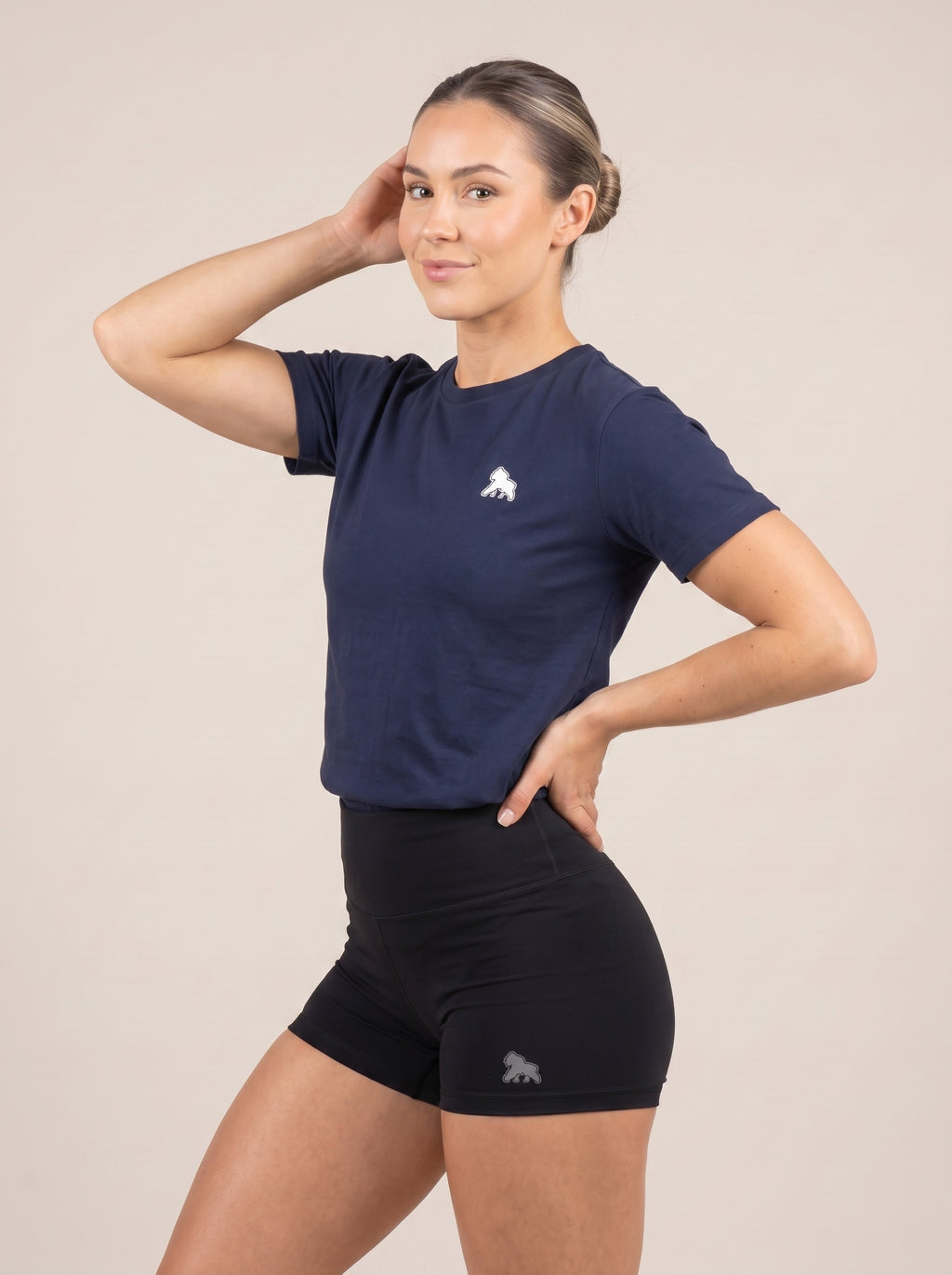 Model in a navy FIT APE women's training tee, angled view with one hand on her hip