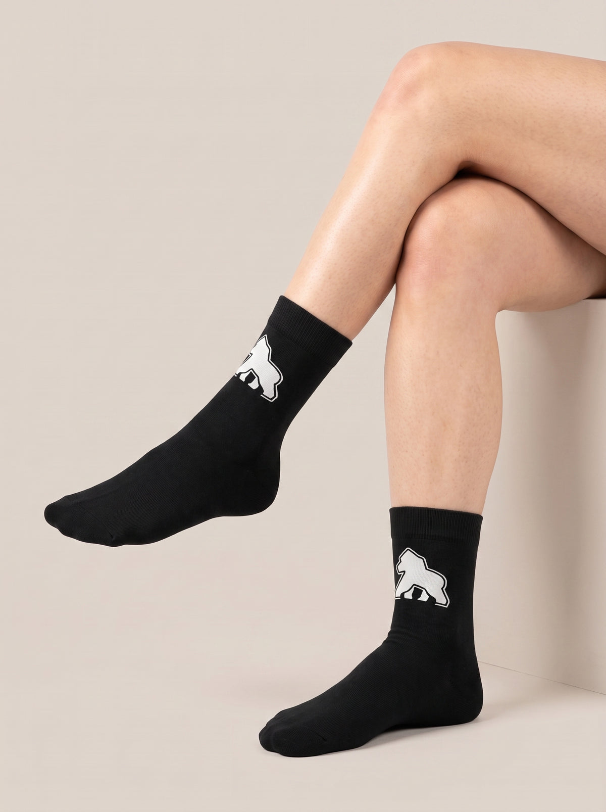 Seated model wearing black FIT APE crew socks with white gorilla emblems