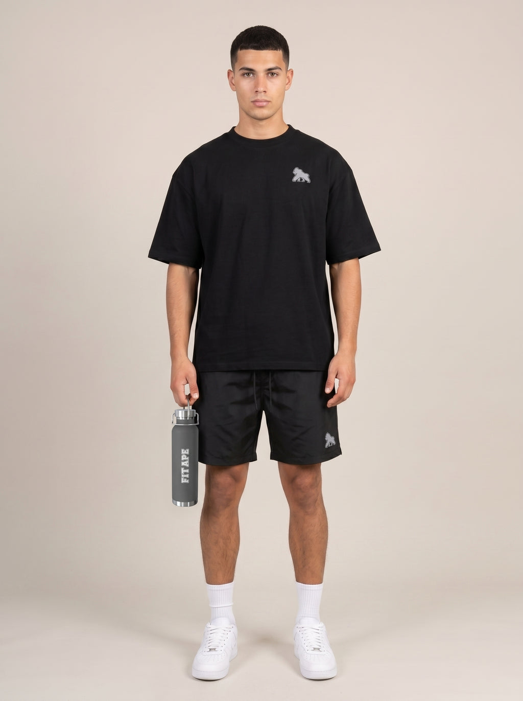 Full-length model in a black tee and shorts holding a gray FIT APE water bottle