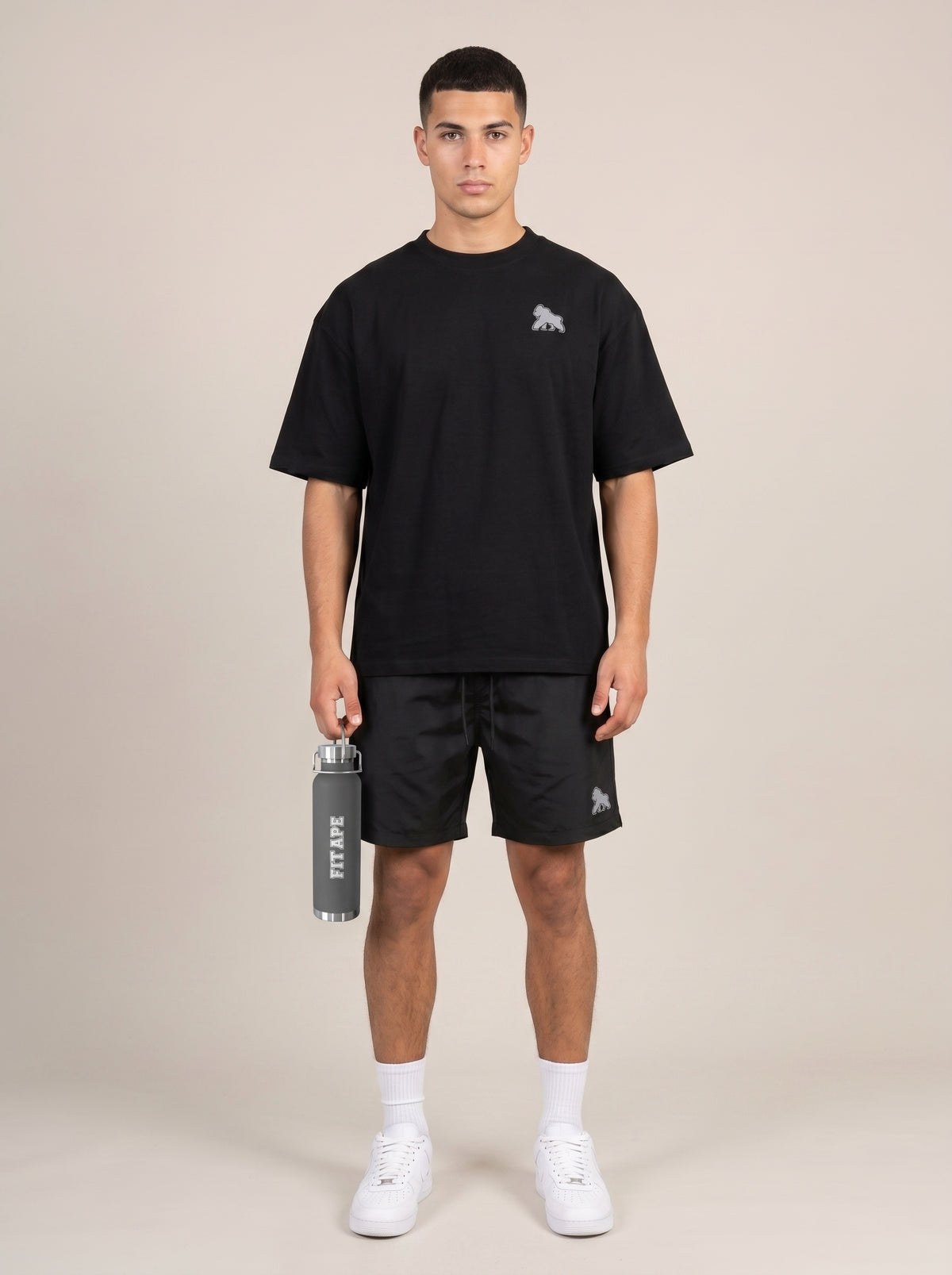 Full-length model in a black tee and shorts holding a gray FIT APE water bottle