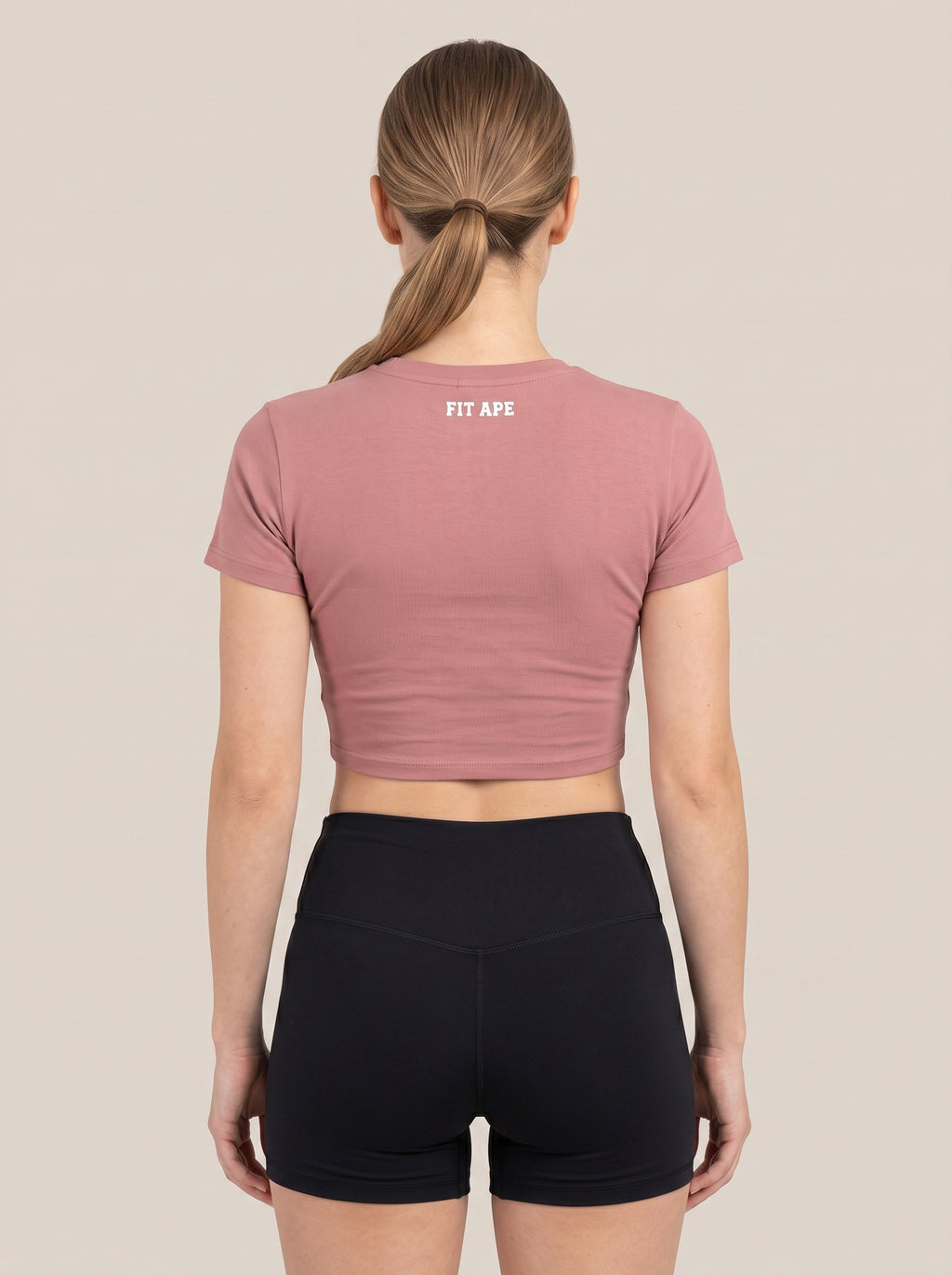 Pink FIT APE women's cropped performance top on a model, back view with neck lettering