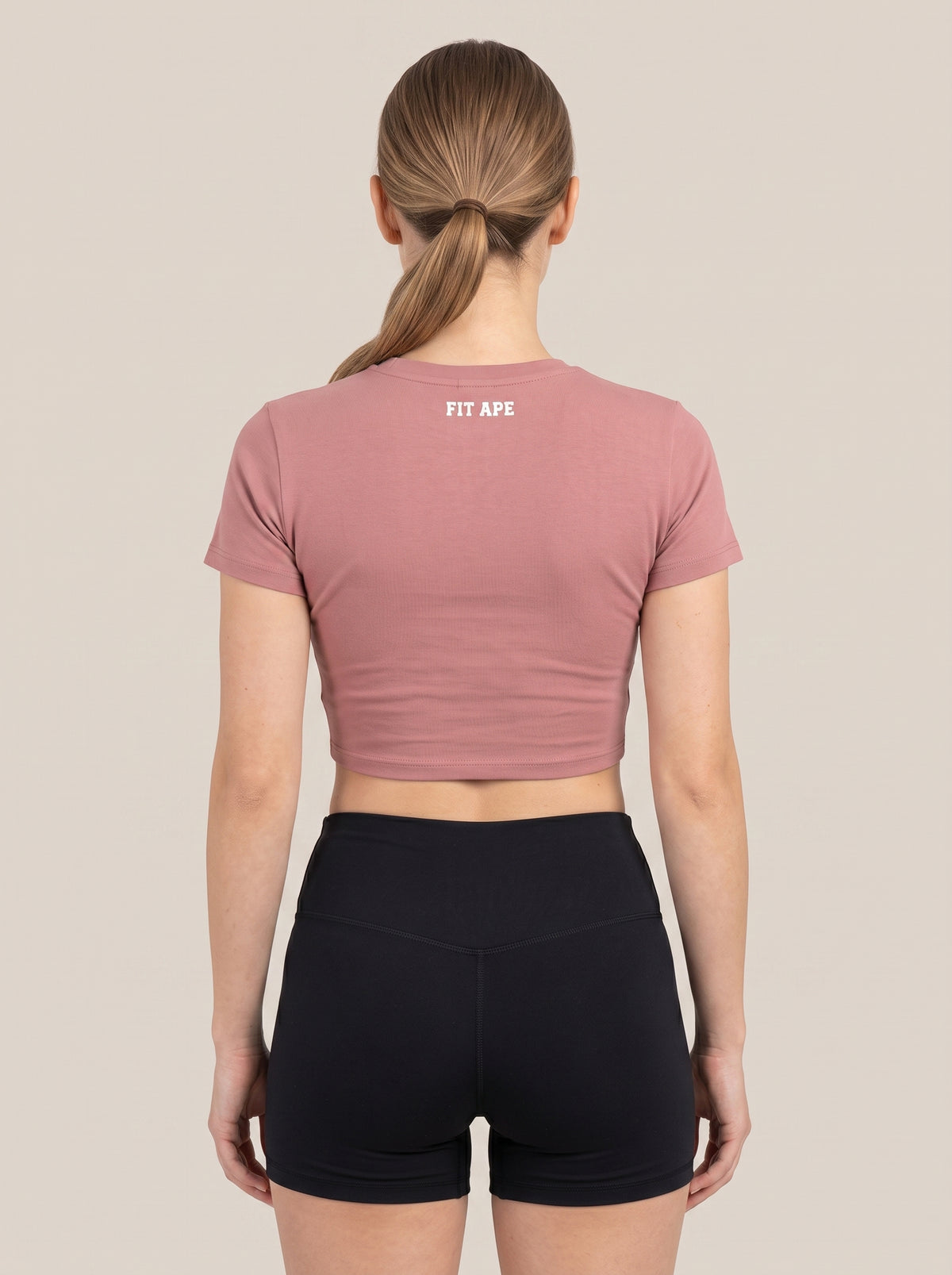 Pink FIT APE women's cropped performance top on a model, back view with neck lettering