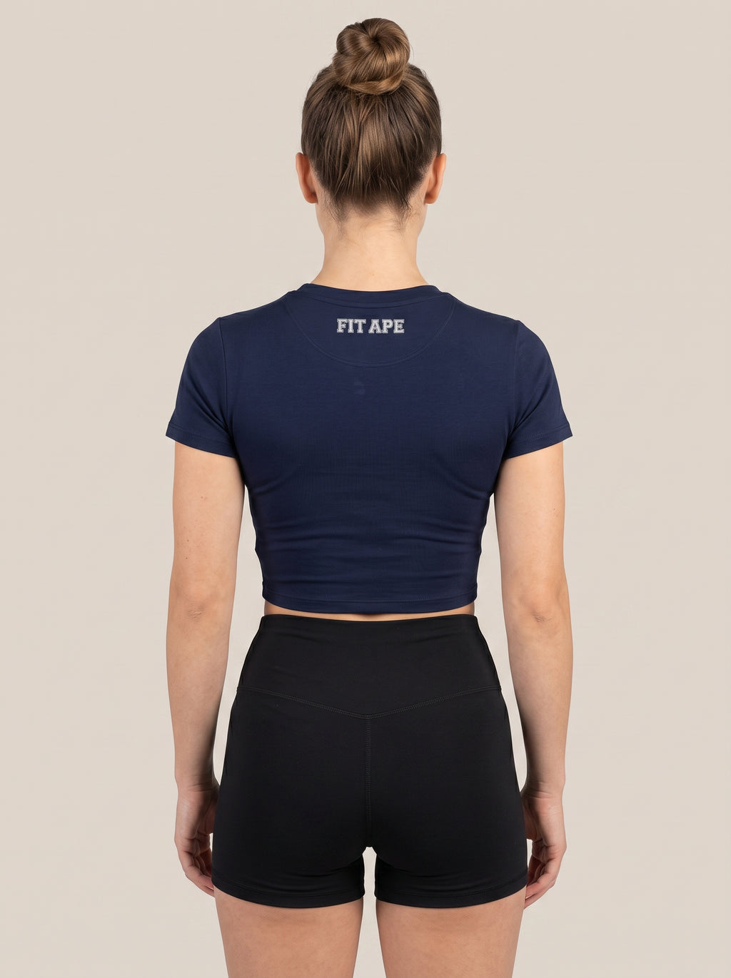 Navy FIT APE women's cropped performance top on a model, back view with neck lettering