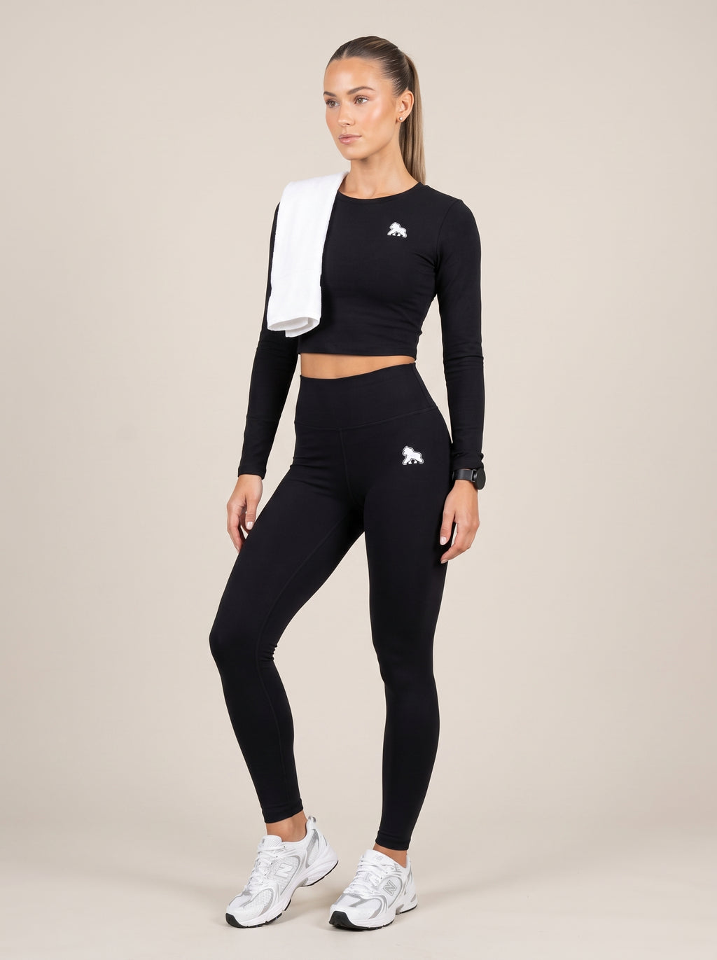 Model wearing a black FIT APE compression crop top with a white towel over one shoulder