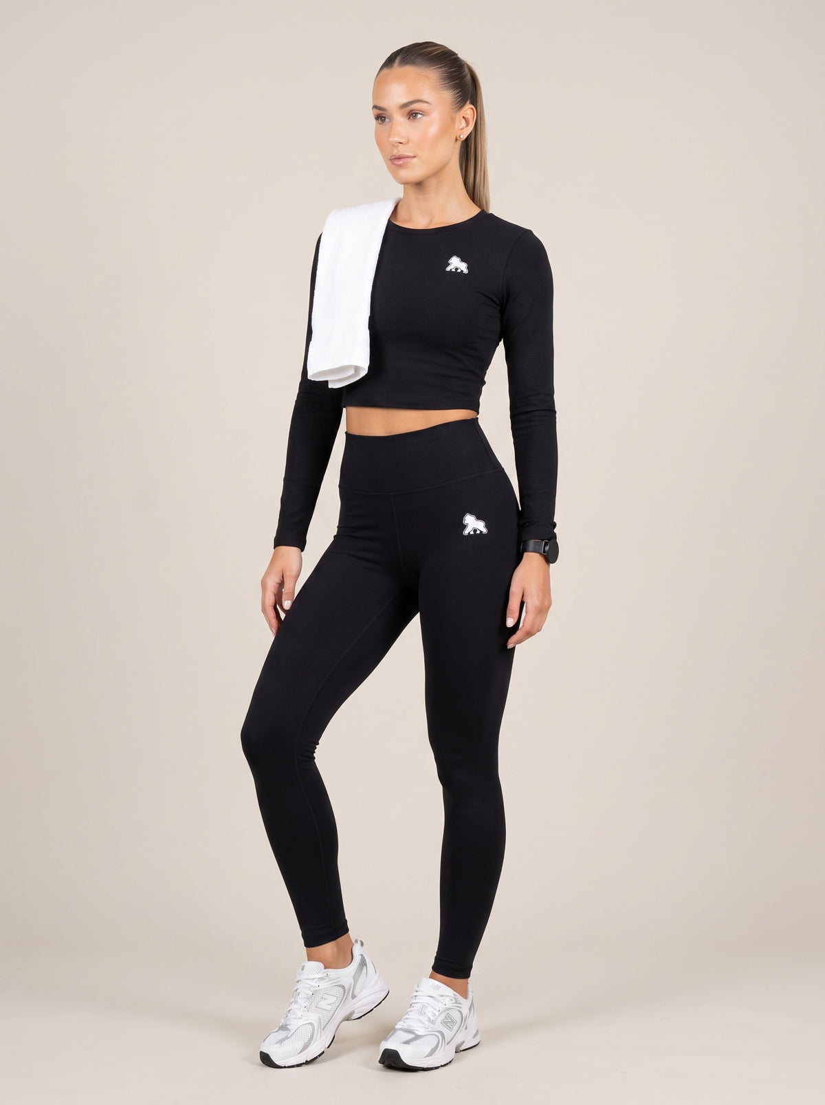 Model wearing a black FIT APE compression crop top with a white towel over one shoulder