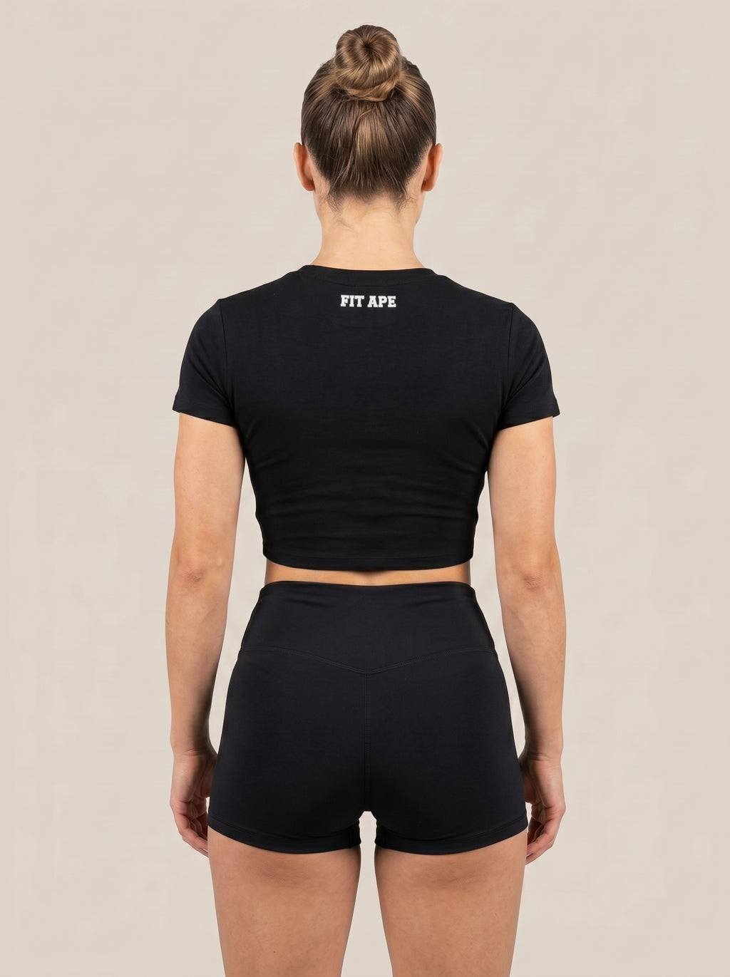 Black FIT APE women's cropped performance top on a model, back view with neck lettering