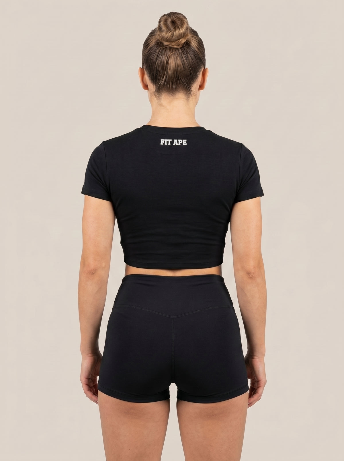 Black FIT APE women's cropped performance top on a model, back view with neck lettering