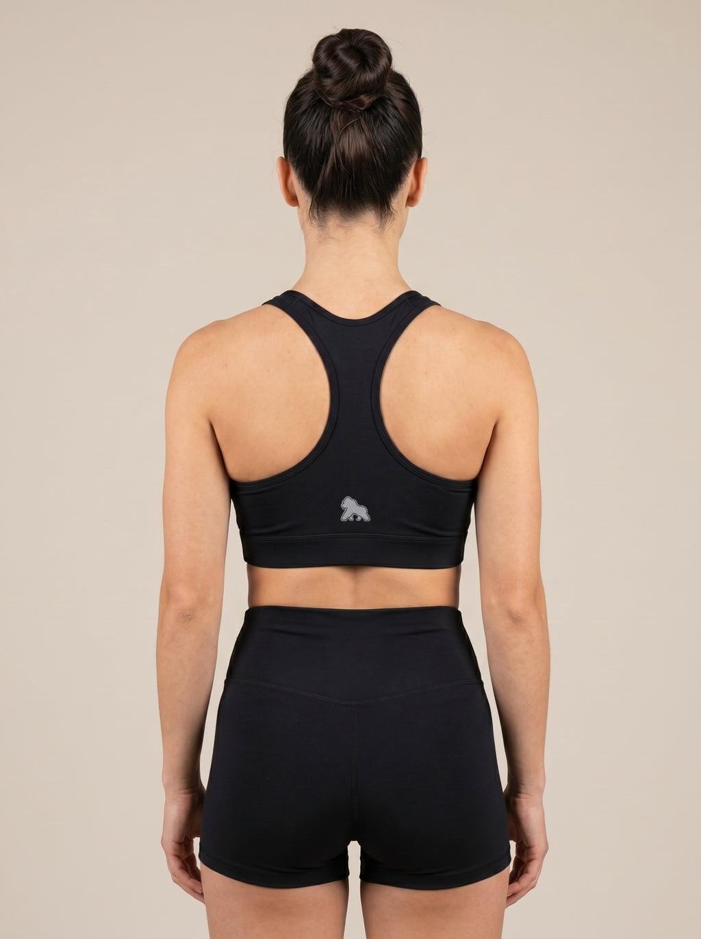 Model wearing a black FIT APE sports bra, back view showing the racerback cut