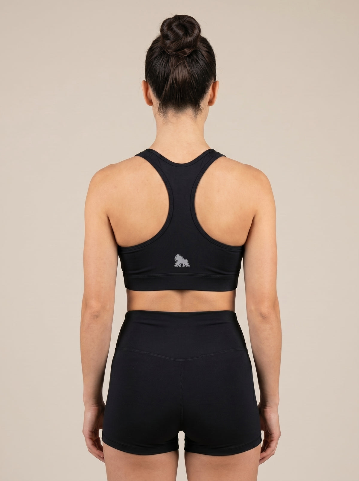 Model wearing a black FIT APE sports bra, back view showing the racerback cut