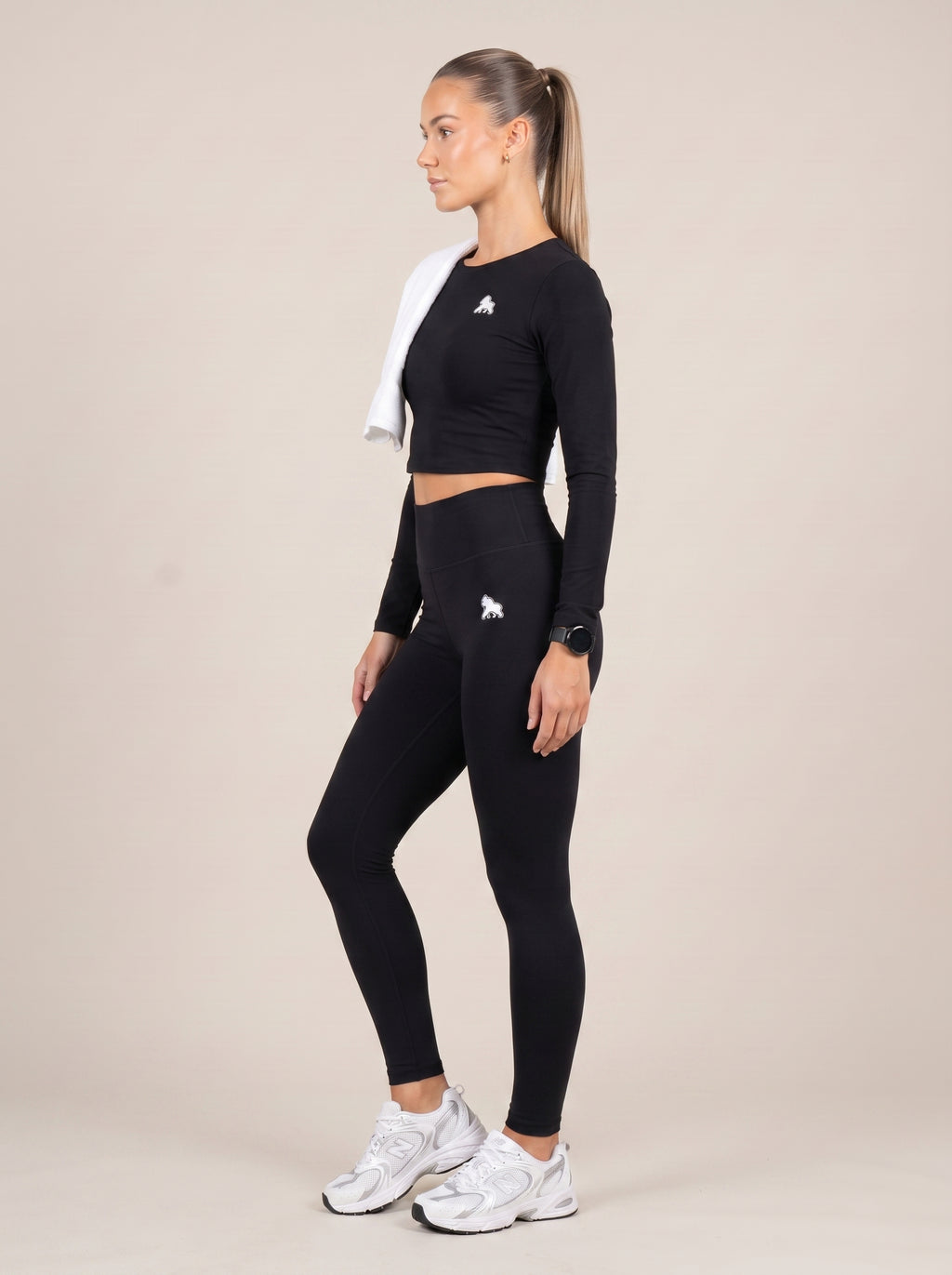 Black FIT APE women's compression crop top on a model with a shoulder towel, side view