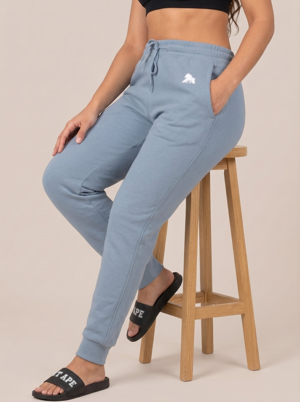 Model seated on a stool wearing black FIT APE slides and blue joggers