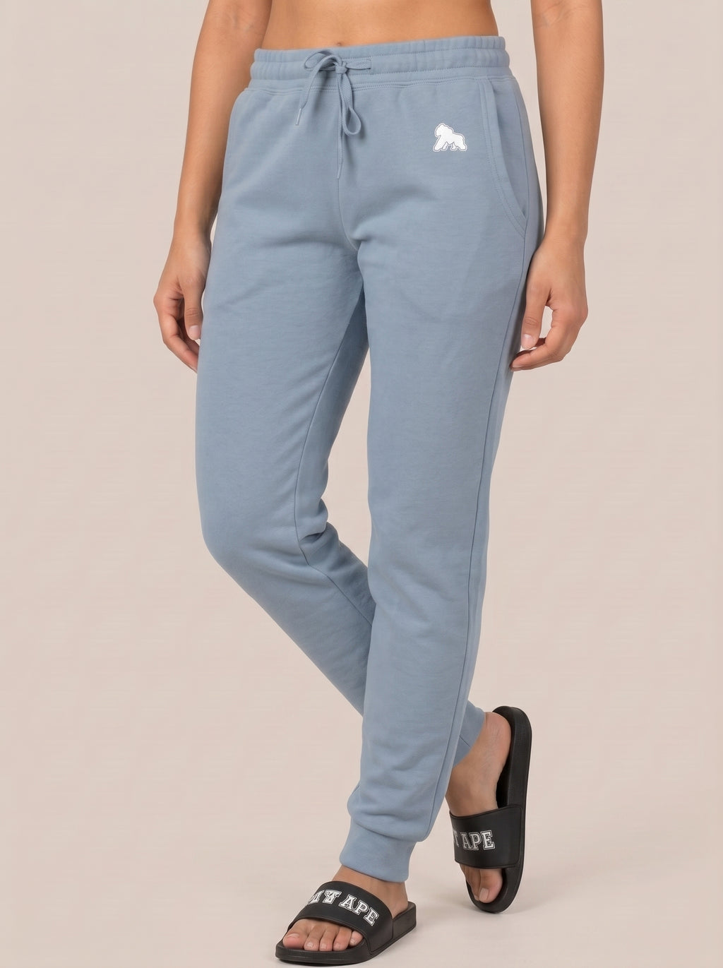 Model standing with crossed ankles in black FIT APE slides and blue joggers