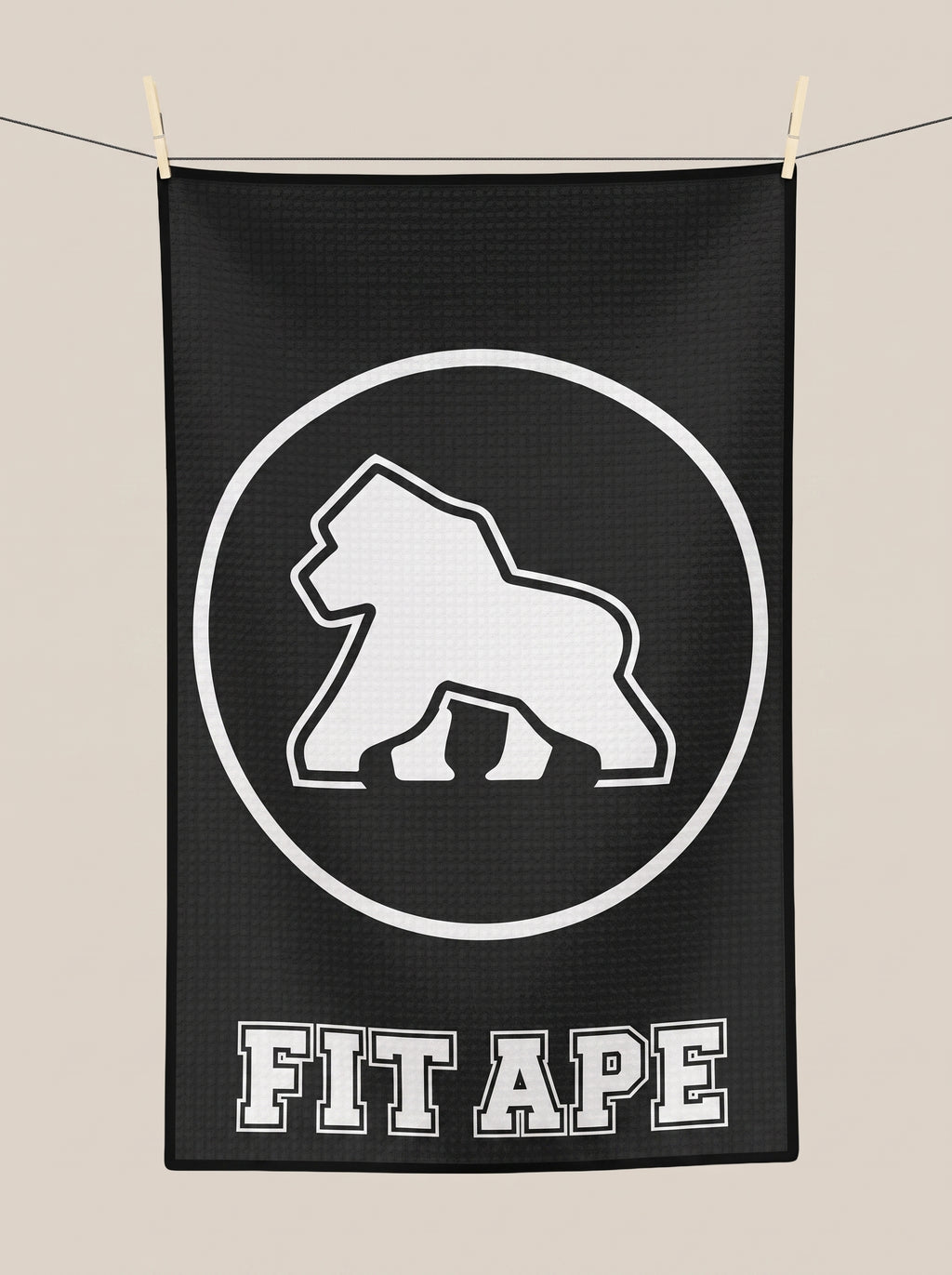Black FIT APE gym towel hanging from a line, showing its white gorilla emblem