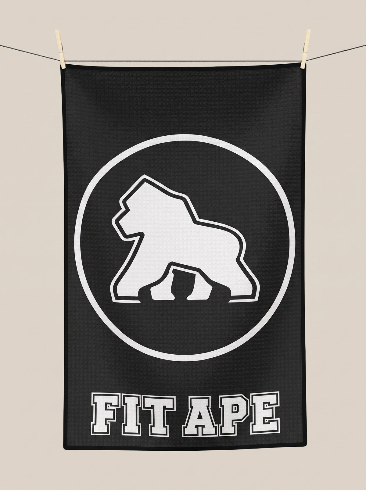 Black FIT APE gym towel hanging from a line, showing its white gorilla emblem